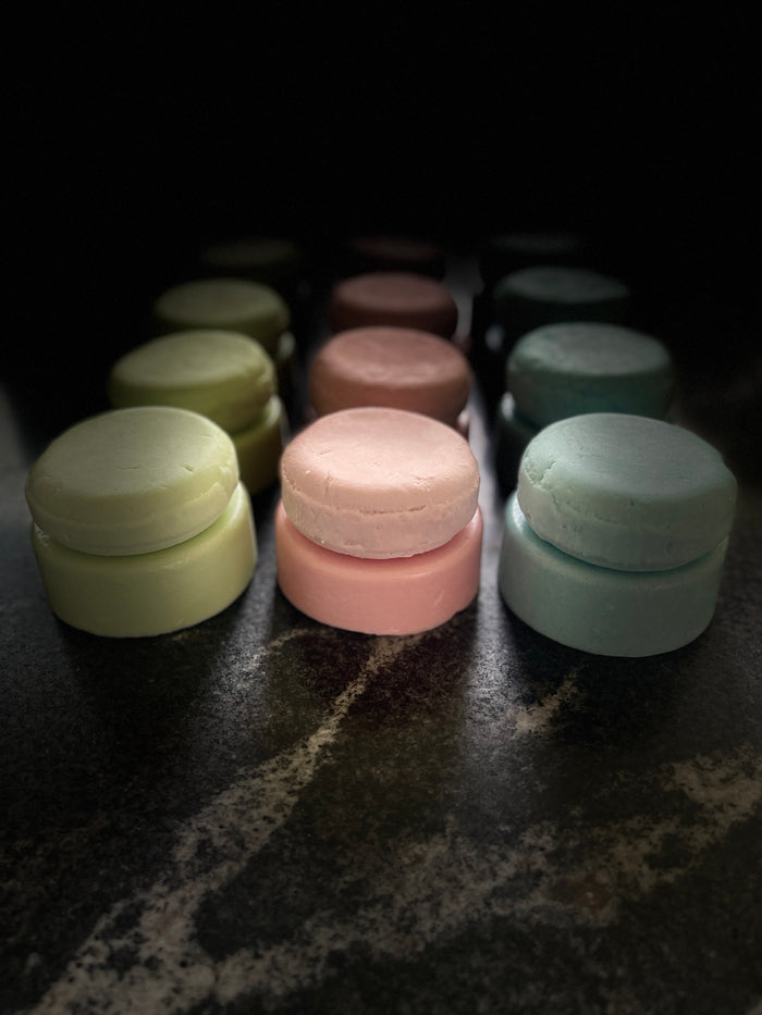 Three rows of green, pink, and blue conditioner and shampoo bars layered on each other, sitting on a dark marbled surface