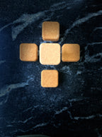 Five small square face soap arranged in a cross pattern on a dark marbled surface.