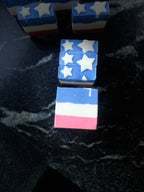 Three small square layered bars with a red, white, and blue color scheme and white star details, arranged on a dark marbled surface.