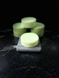 Pale green round Baja Breeze conditioner bars arranged on a dark marble surface, with one bar in the foreground resting on a gray square block and the others stacked behind it against a black background.