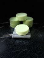 Pale green round Baja Breeze conditioner bars arranged on a dark marble surface, with one bar in the foreground resting on a gray square block and the others stacked behind it against a black background.