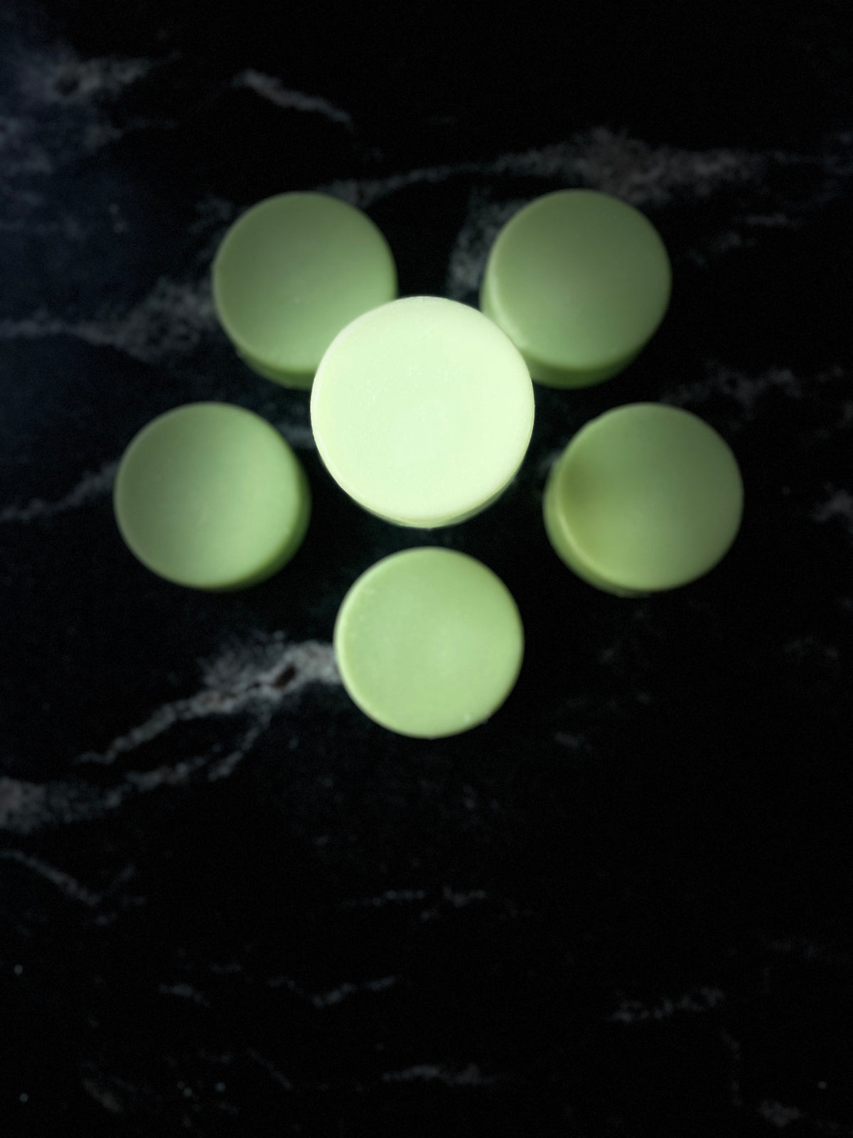 Pale green round Baja Breeze conditioner bars arranged in a flower-like pattern on a dark marbled surface