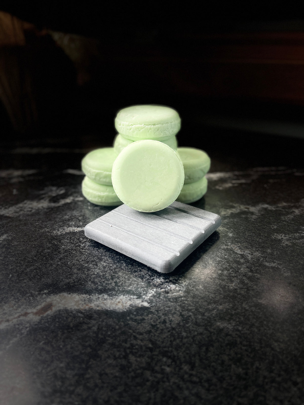 Four pale mint green shampoo bars arranged on a dark stone surface, with one bar standing upright on a gray rectangular block in the foreground.