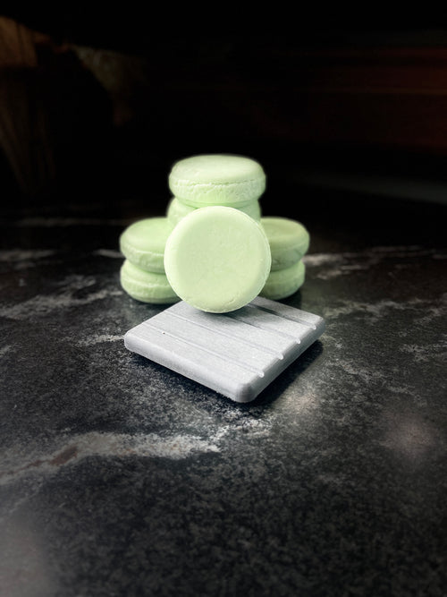 Four pale mint green shampoo bars arranged on a dark stone surface, with one bar standing upright on a gray rectangular block in the foreground.