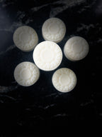Six off-white soap arranged in a circle with one in the center highlighted. The soap is created with a flower mold