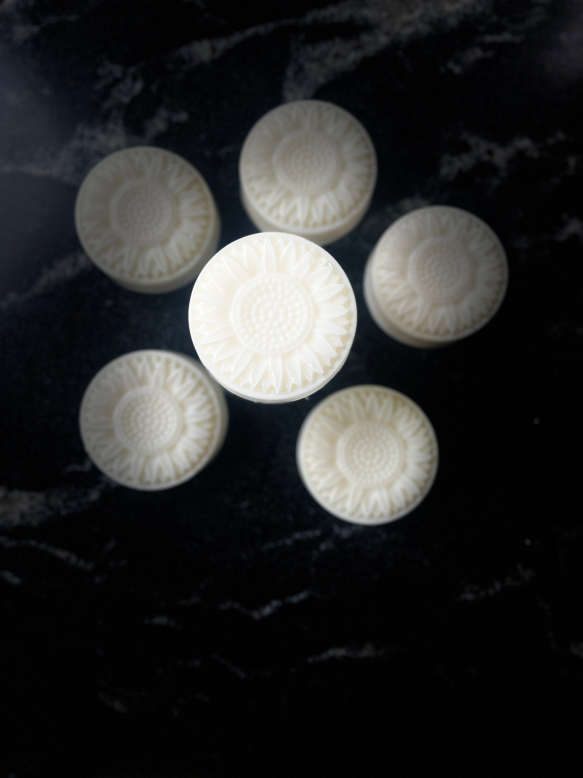 Six off-white soap arranged in a circle with one in the center highlighted. The soap is created with a flower mold