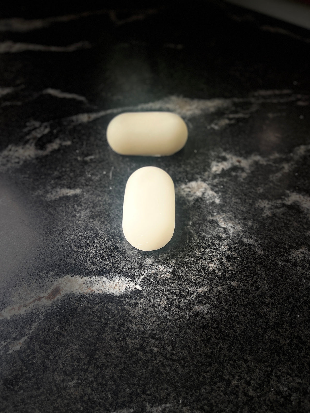 Two oval shaped soaps on a dark marbled surface