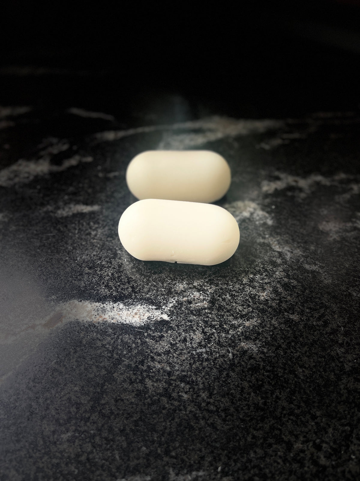 Two oval shaped soaps arranged on a dark marbled surface
