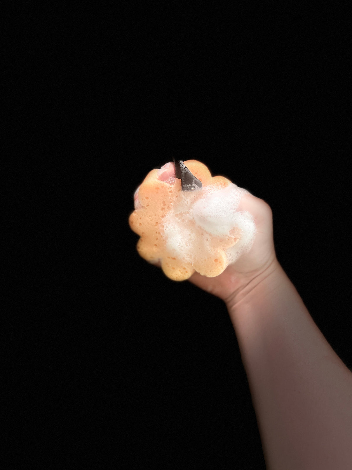 A hand holding a squishy, flower-shaped foam bath sponge against a solid black background.