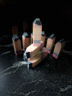 A set of novelty pencil-shaped soaps standing upright on a dark, textured surface against a black background.