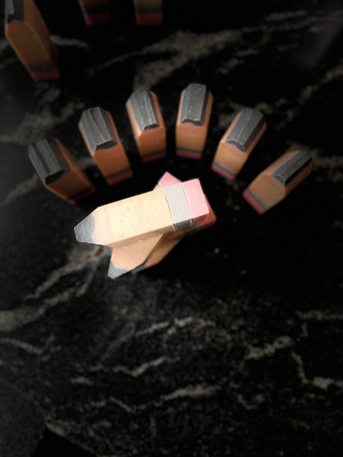 A set of small chunky soap pencils arranged on a dark marbled surface, with another stack of pencils lying on their side