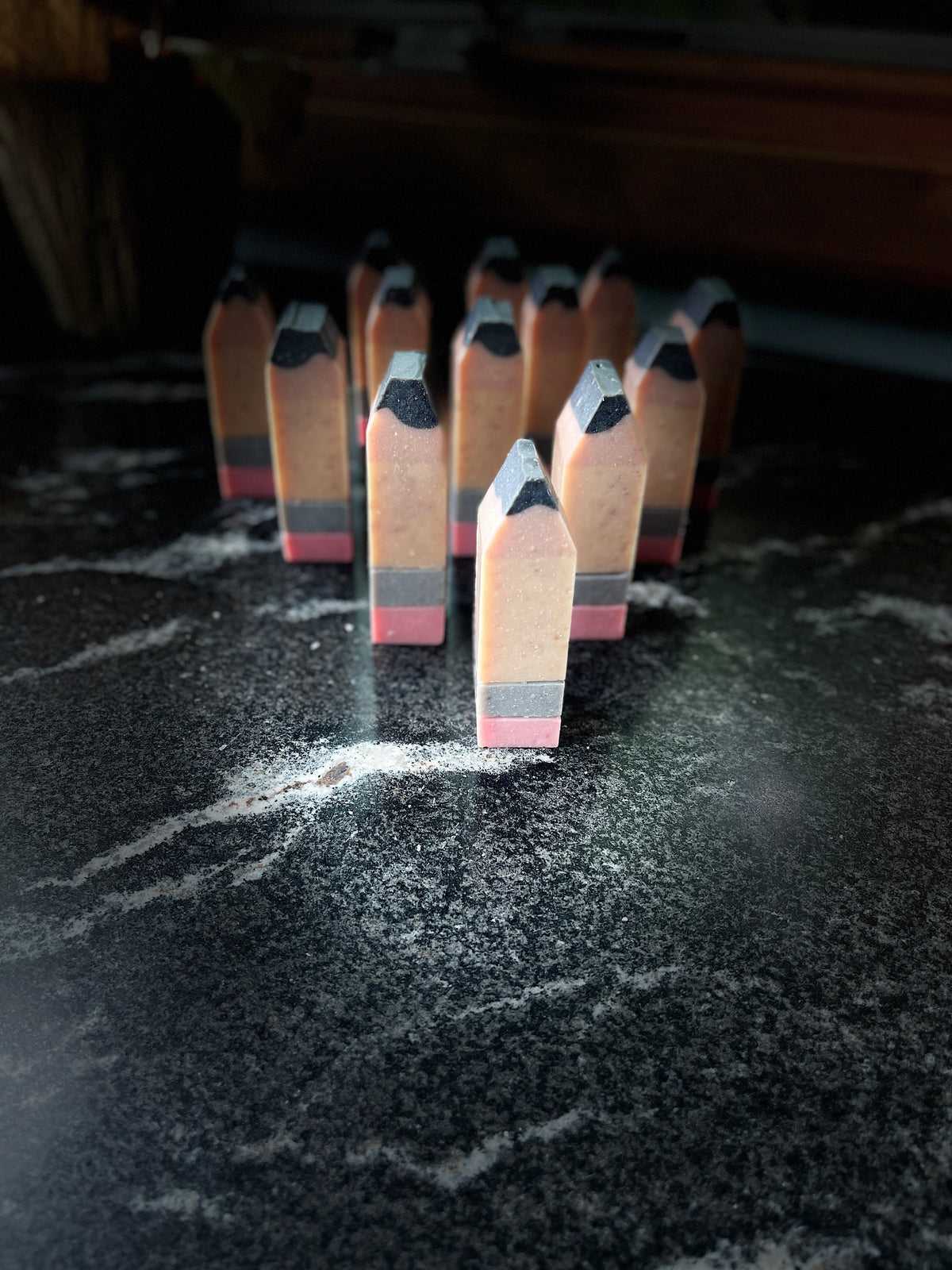 A set of miniature wooden pencils standing upright on a dark, marbled surface