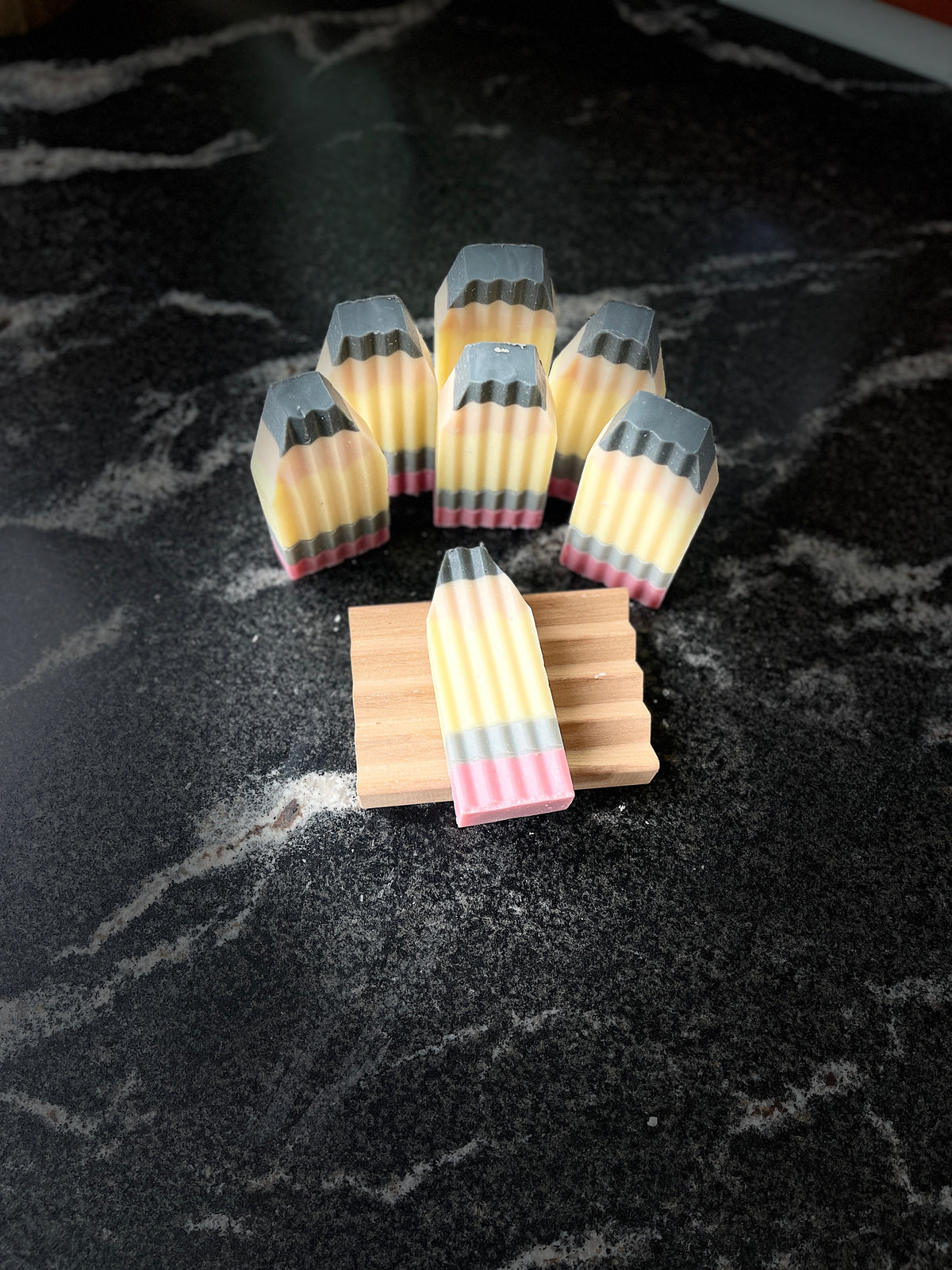 Six crinkle cut pencil-shaped soaps arranged on a black marble surface, with one soap laying on a small wooden soap dish in the foreground.