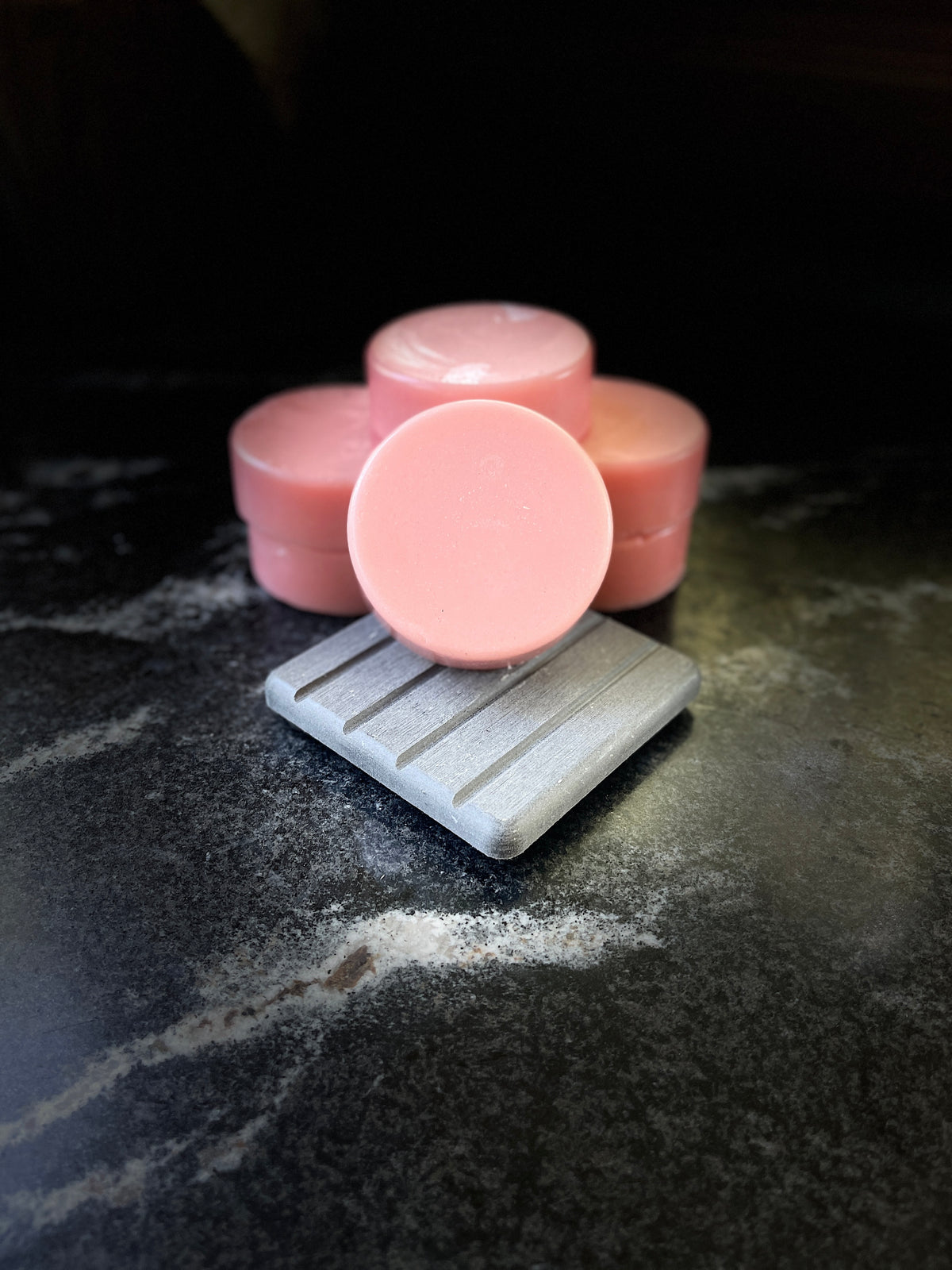 Multiple crystal sands pink round conditioner bars displayed on a marble surface, with one bar resting on a gray soap dish in the foreground.