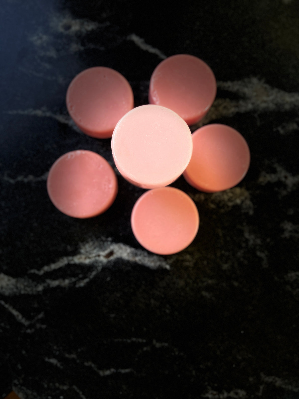 Six crystal sands pink round conditioner bars, arranged in a flower pattern on a dark black marble surface.