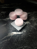 Crystal sands round shampoo bars arranged on a dark marble surface, with one resting on a small gray square dish and the others grouped behind it on a dark marbled surface