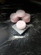 Crystal sands round shampoo bars arranged on a dark marble surface, with one resting on a small gray square dish and the others grouped behind it on a dark marbled surface