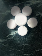 Six round pink crystal sands shampoo bars arranged in a flower-like cluster on a dark marbled surface.