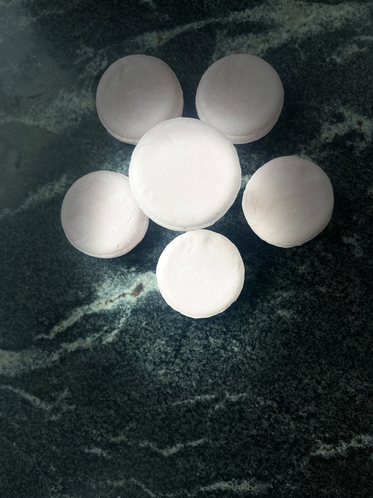 Six round pink crystal sands shampoo bars arranged in a flower-like cluster on a dark marbled surface.