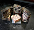 Several marbled artisan soap bars with tiger swirls of cream, brown, and dark, arranged on a dark stone surface.