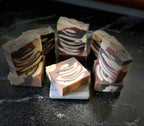 Several marbled artisan soap bars with tiger swirls of cream, brown, and dark, arranged on a dark stone surface.