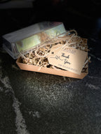 A small kraft paper gift box filled with shredded paper and a hanging tag that reads 'Thank You FOR YOUR BUSINESS,' photographed on a dark textured surface.