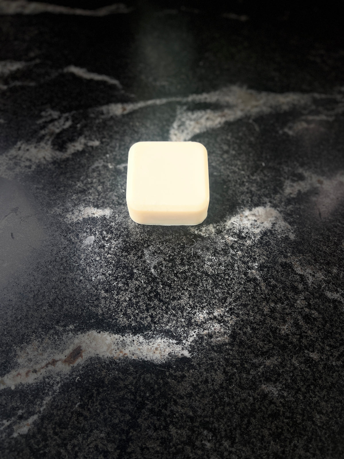 One single square bar of soap on a dark marbled surface