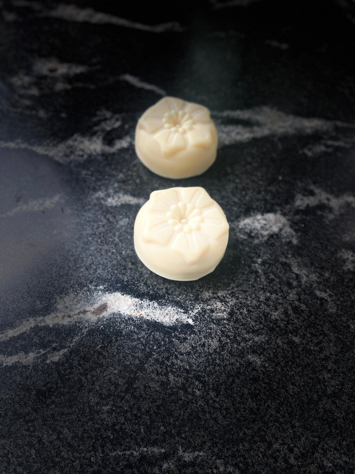 Two round flower shaped soaps on a dark marbled surface