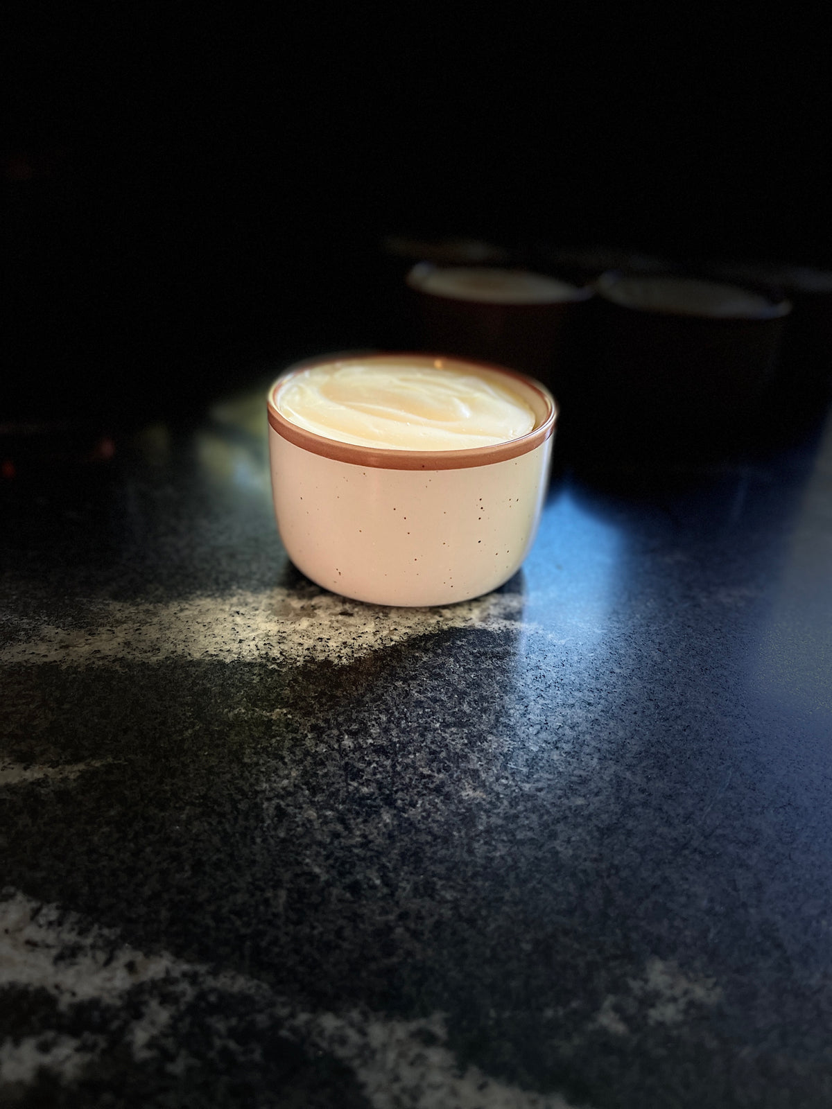 A speckled ceramic cup with a warm brown rim, filled with solid dish soap, set on a dark textured countertop