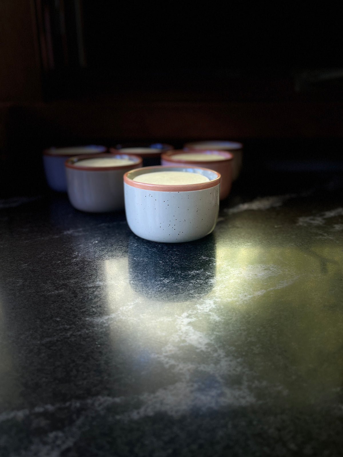 A speckled ceramic bowl with a warm brown rim, filled with solid dish soap set on a dark textured surface against a black background.