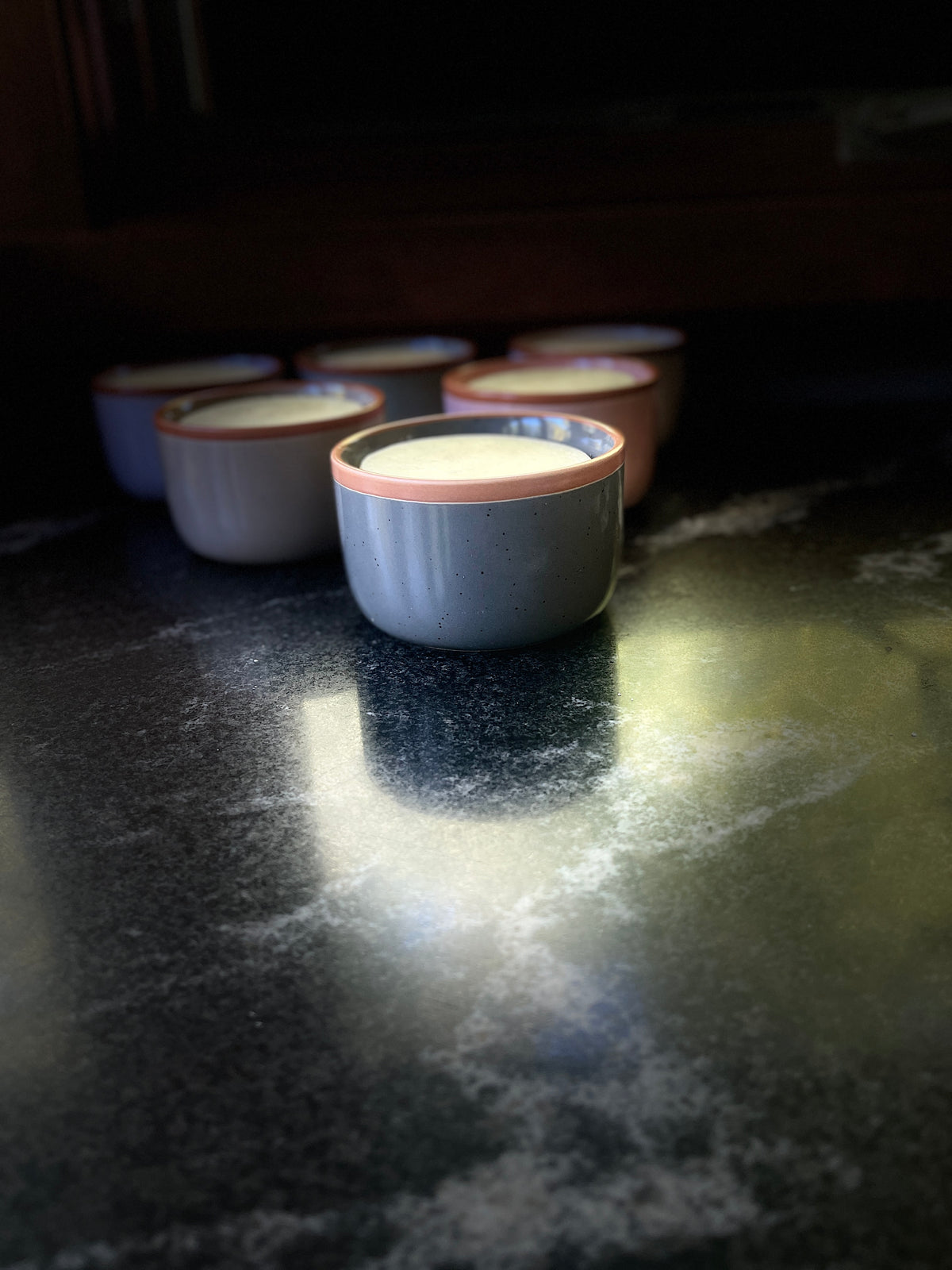 A speckled ceramic bowl with a warm brown rim, filled with solid dish soap set on a dark textured surface against a black background.