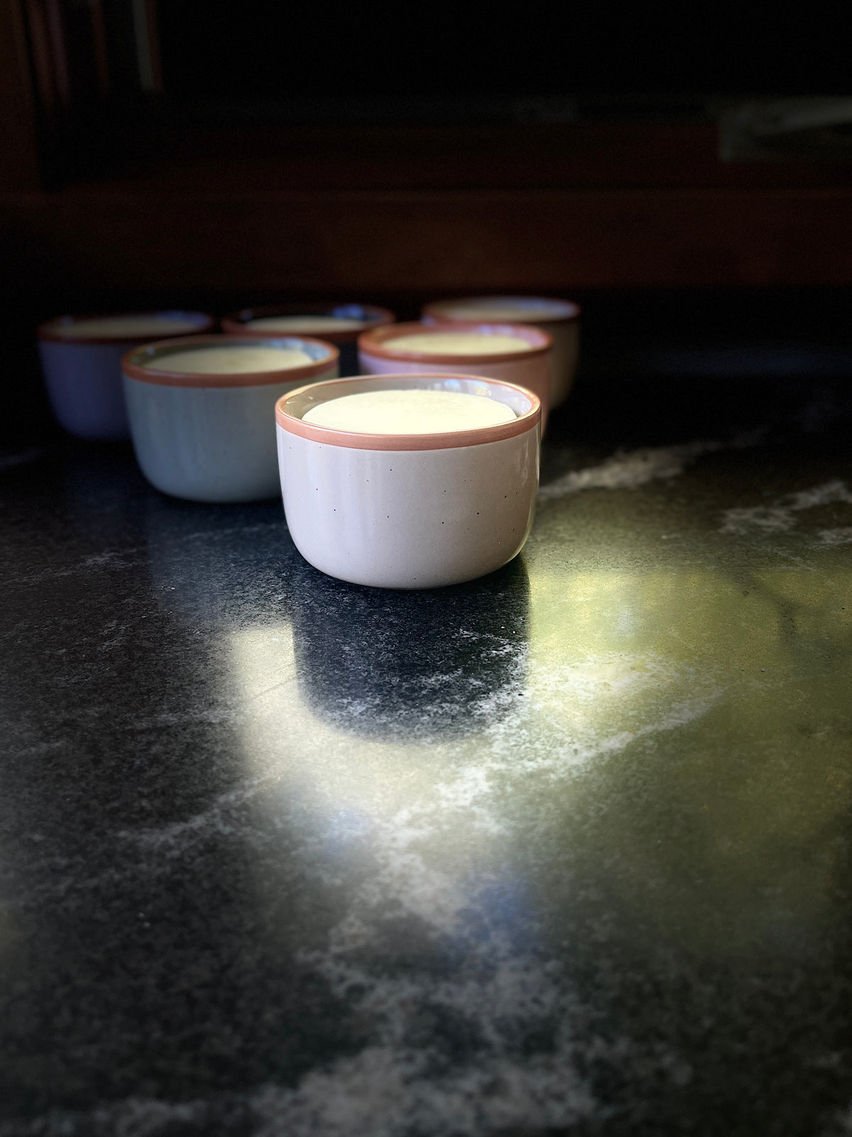 A speckled ceramic bowl with a warm brown rim, filled with solid dish soap set on a dark textured surface against a black background.