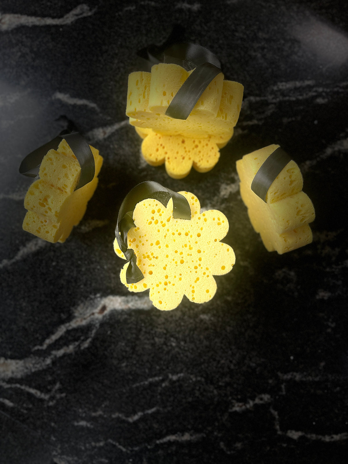Several yellow soap sponge with black ribbon handles arranged on a dark textured surface