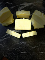 Several pale yellow bars of soap arranged on a dark marbled surface, with the center bar stamped with the brand name SAVI SUDS.