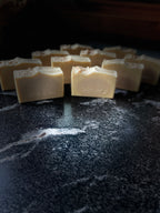 Several rectangular bars of pale beige soap with SAVI SUDS stamped on the front, arranged on a dark marble-like surface with a shallow depth of field.