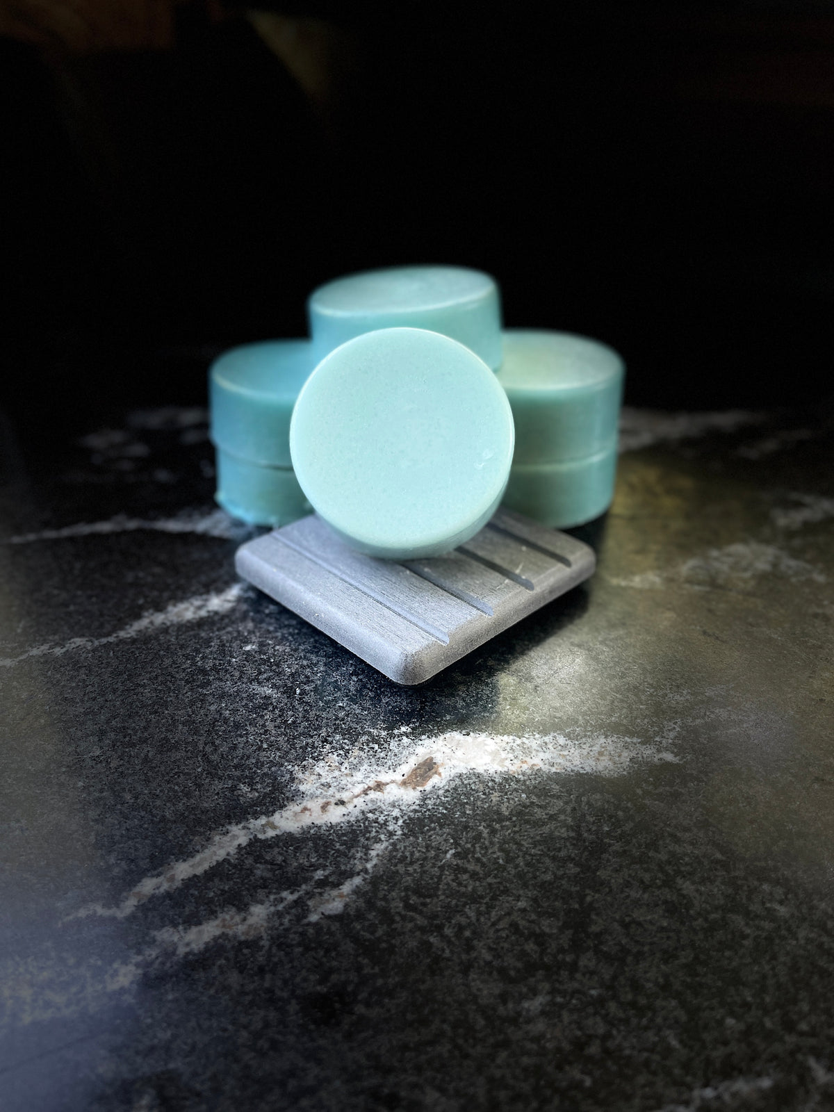 Multiple ocean orchid round blue conditioner bars arranged on a dark marble surface, with one standing upright on a small gray stone dish