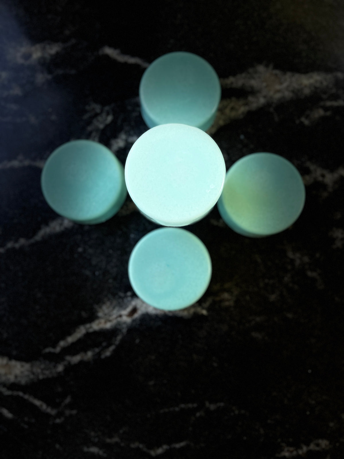 Five blue round ocean orchid conditioner bars arranged in a flower pattern on a black marble surface