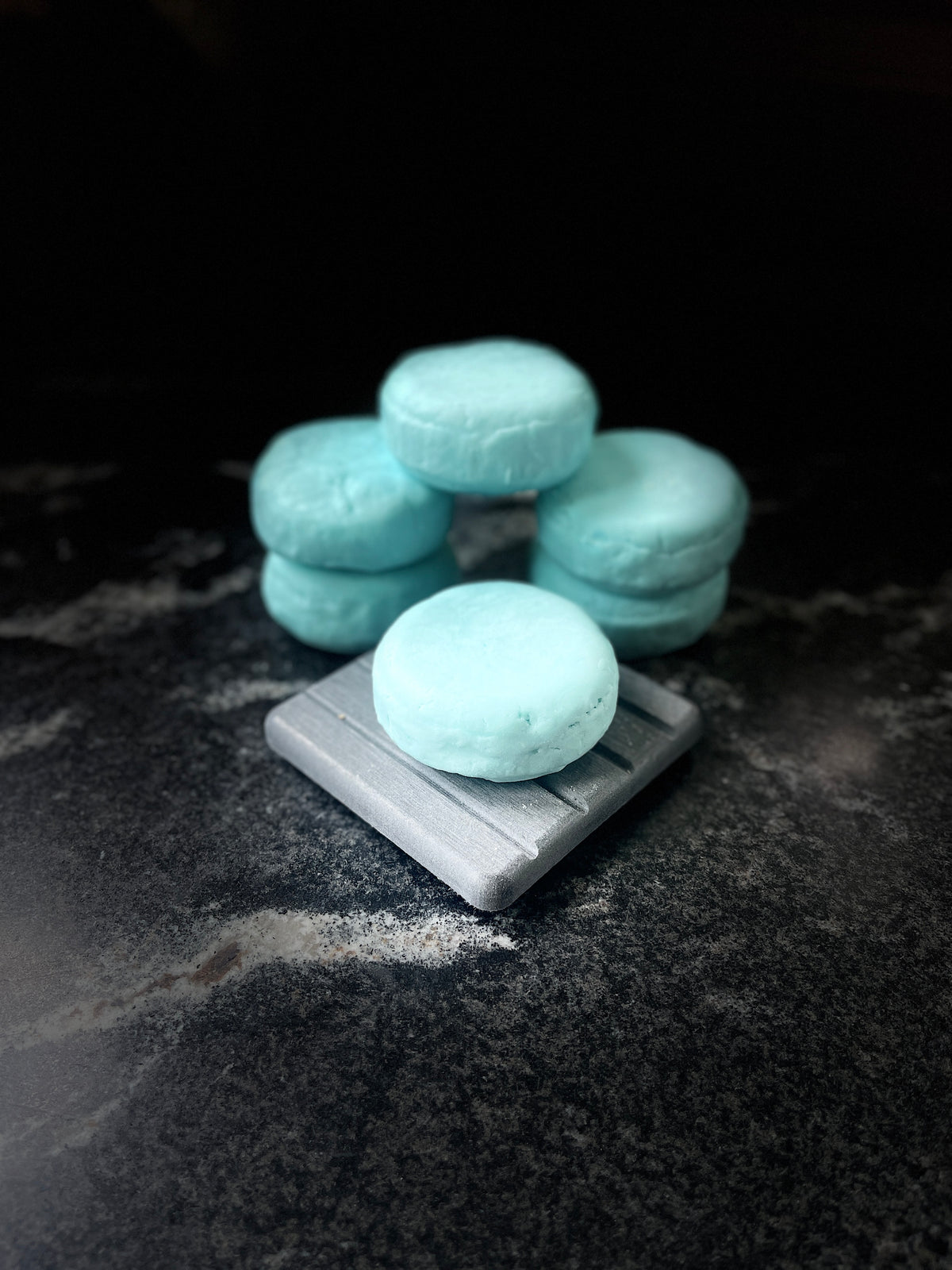 Ocean Orchid round shampoo bars arranged on a marbled surface with one bar in front on top on a squared gray stone plate