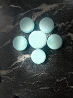 six light blue round Ocean Orchid shampoo bars arranged in a flower-like pattern on a dark marbled surface.