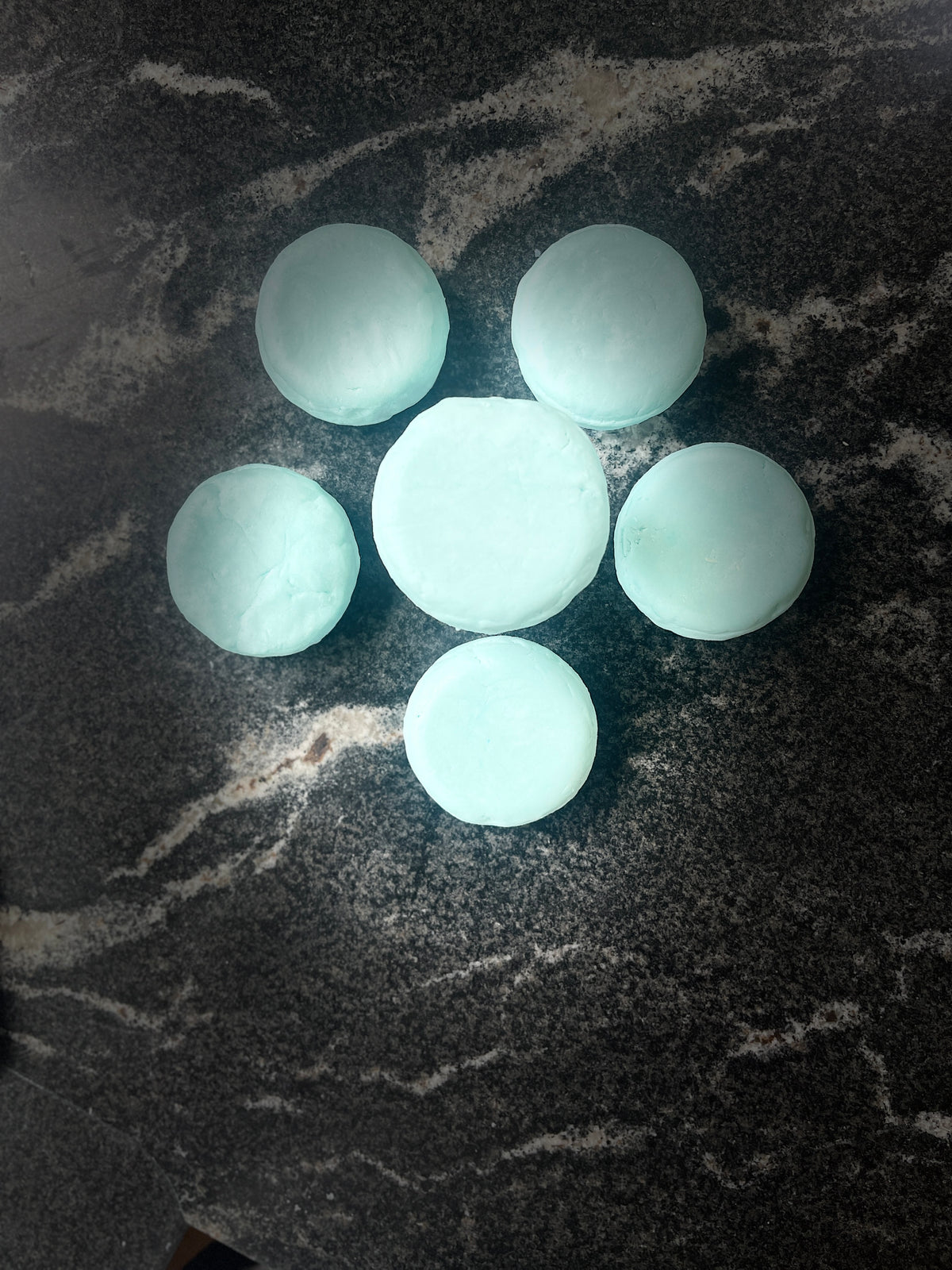six light blue round Ocean Orchid shampoo bars arranged in a flower-like pattern on a dark marbled surface.