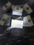 Several handmade soap bars with a cream-colored textured top and a dark  onyx stone inlay, arranged on a dark gray marble surface. The center soap bar is upright and shows the brand name 'Savi Suds' and 'Onyx'.