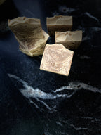 Several handmade soap bars with a marbled beige and brown swirl pattern, arranged on a dark black marble surface. One bar in the foreground is embossed with the brand name 'SAVI SUDS'.
