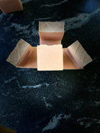Several square bars of Savi Suds Patchouli Dawn handmade soap arranged on a dark marble surface, with one bar centered and the others fanned out around it.