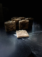 Several artisanal soap bars with a swirled beige and dark brown pattern, arranged on a dark, textured surface with one bar in the foreground.