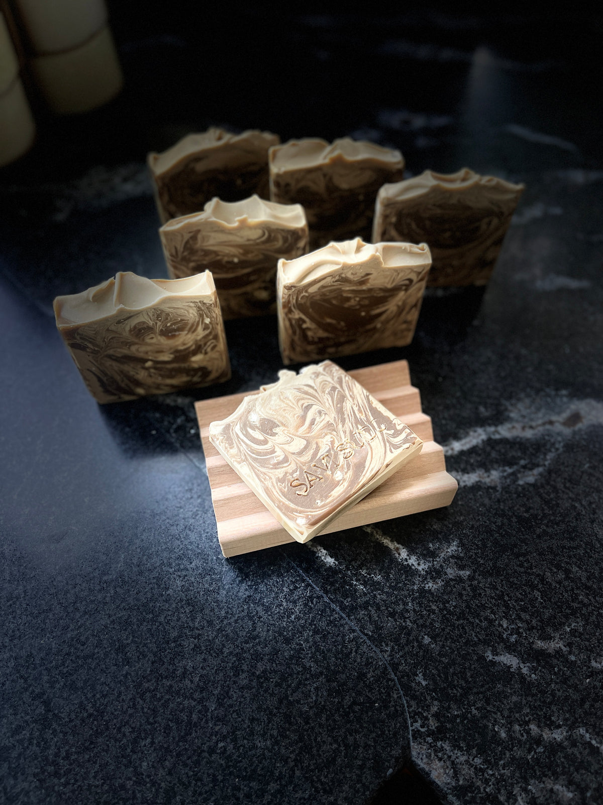 Handcrafted artisan soap bars with a brown and beige swirl pattern, displayed on a dark surface with one bar resting on a wooden block in the foreground