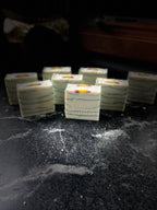 Several square bars of handmade soap with white layers, blue mica line, and a pencil embed on top. Soap is arranged on a dark marble surface