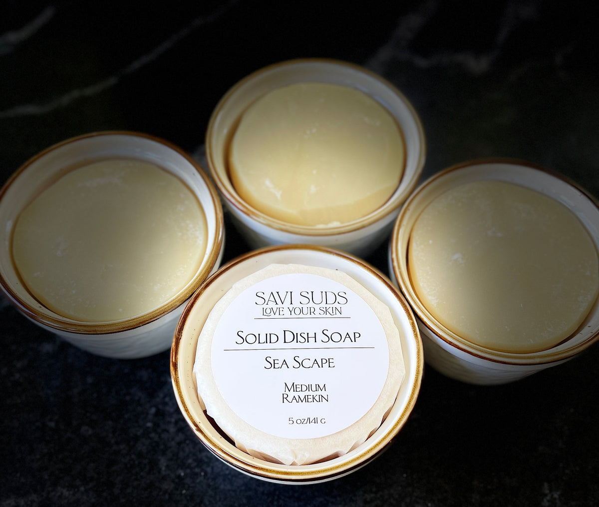 Solid Dish Soap in ramekins with brown rim. Foreground picture has a wrapped soap with Savi Suds Sea Scape scent
