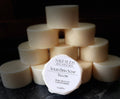 A stack of cream-colored solid dish soap bars arranged in a pyramid, with one bar in the front displaying its white paper label that reads 'SAVI SUDS SOLID DISH SOAP TALLOW'. The soaps are photographed on a dark, textured countertop against a dark background.