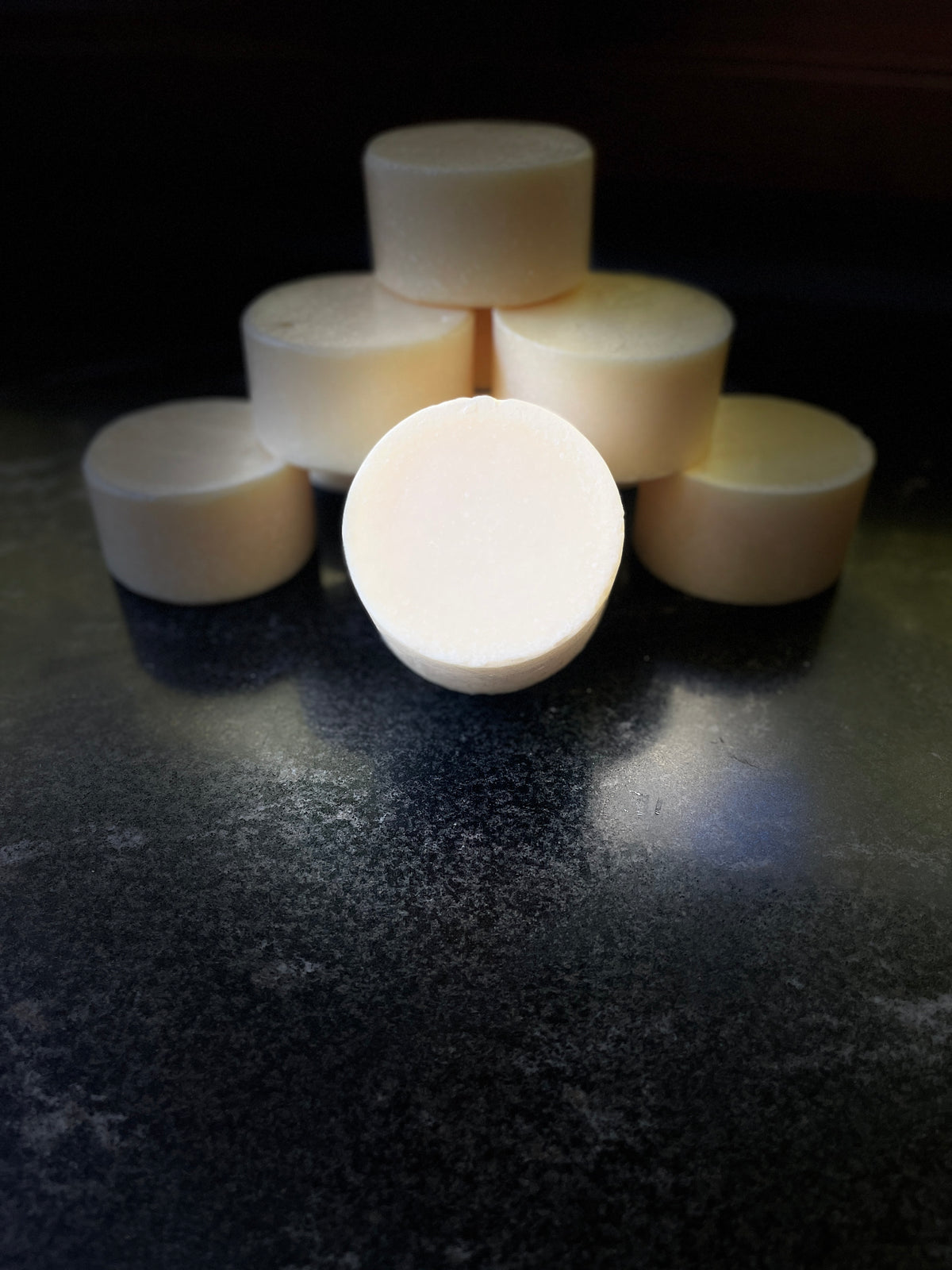 Multiple solid dish soap pucks arranged in a pyramid on a dark, reflective surface, with one soap bar standing upright in the center.