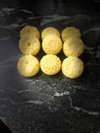 Nine pale yellow, flower-shaped handmade soaps arranged in a 3x3 grid on a dark, polished marble surface.